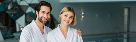 Cheerful man in bathrobe hugging girlfriend in spa center, bannerの写真素材
