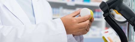 cropped view of pharmacist in white coat scanning bottle with medication, bannerの写真素材