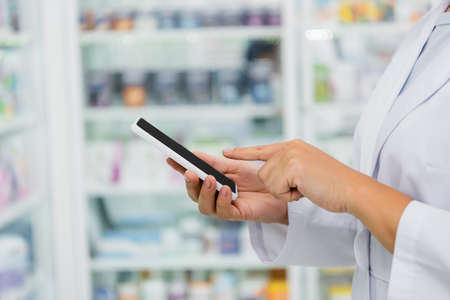 cropped view of pharmacist in white coat pointing at smartphoneの写真素材