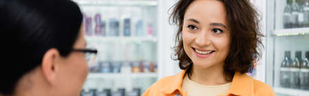 brunette woman smiling while looking at blurred pharmacist in drugstore, bannerの写真素材