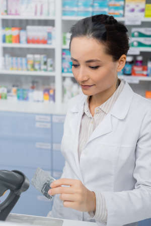 tattooed pharmacist holding blister pack near scanner in drugstoreの写真素材