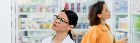 asian pharmacist in glasses near blurred customer in drugstore, bannerの写真素材