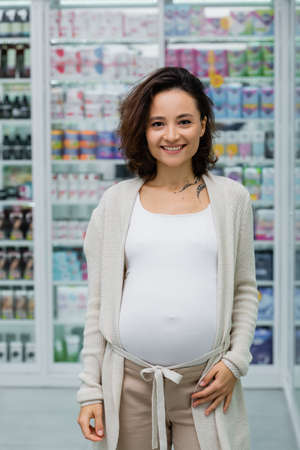 cheerful and pregnant woman with tattoo in drugstoreの写真素材