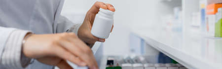 cropped view of pharmacist in white coat holding bottle with medication while opening drawer in drugstore, bannerの写真素材