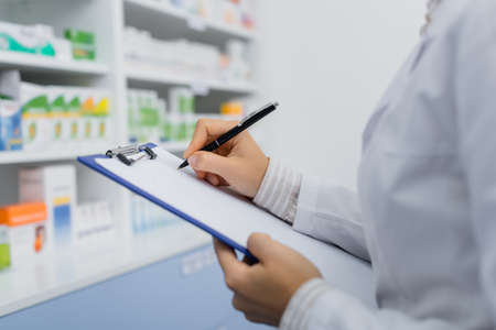 cropped view of pharmacist in white coat writing on clipboardの写真素材
