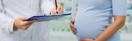 cropped view of pregnant woman standing near pharmacist writing on clipboard, bannerの写真素材