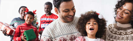 smiling parents near amazed daughter and blurred african american family with christmas presents, bannerの写真素材