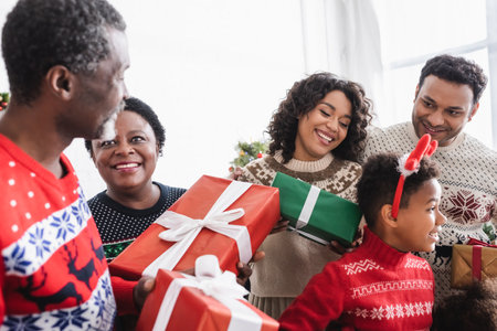 joyful african american family smiling while holding christmas gifts at home