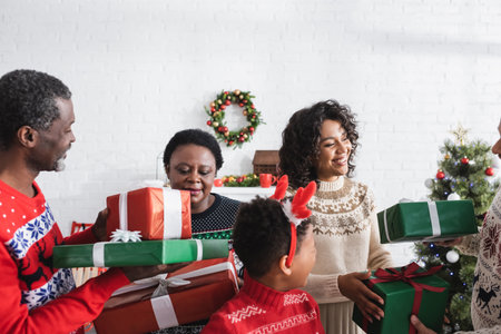 joyful african american parents gifting presents to each other in decorated living room