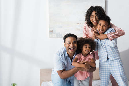 happy african american parents hugging kids while having fun in bedroom in morning