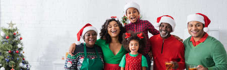 joyful african american family in santa hats looking at camera near christmas tree, bannerの写真素材