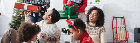 african american family near grandparents with christmas presents in living room, banner