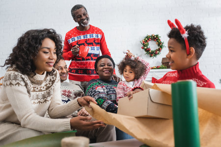 mother and son packing gift box near happy african american familyの写真素材