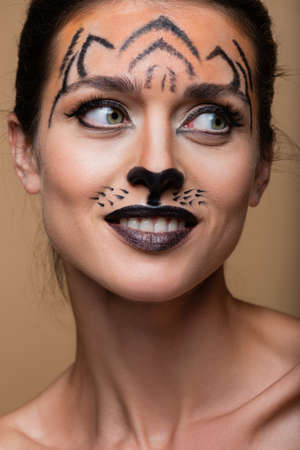 close up of joyful woman with tiger makeup looking away isolated on beigeの写真素材