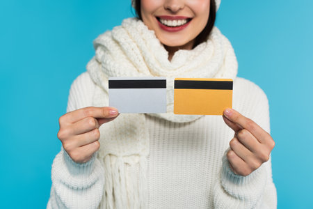 Cropped view of blurred woman in knitted sweater holding credit cards isolated on blueの写真素材