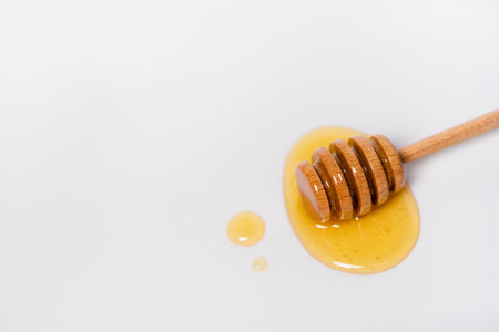top view of wooden dipper near drops of honey on white background with copy space
