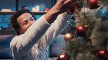 happy african american man in sweater decorating christmas treeの写真素材