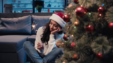 pleased african american woman in santa hat holding sparkler near blurred decorated firの写真素材