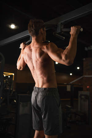 back view of shirtless athletic man training on horizontal bar in sports center
