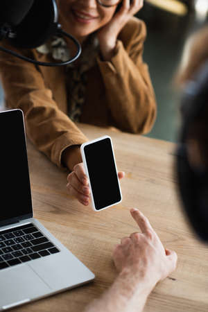 cropped view of blurred radio host pointing at smartphone near cheerful colleagueの写真素材