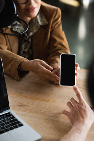 cropped view of blurred announcer pointing at smartphone near colleagueの写真素材