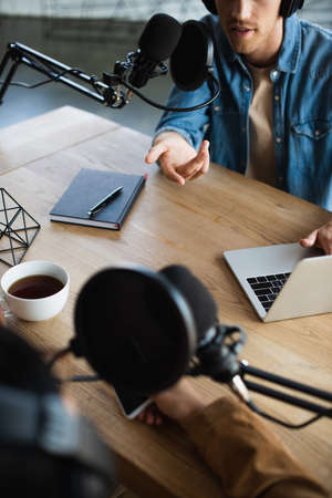 cropped view of radio hosts talking in microphone during podcastの写真素材