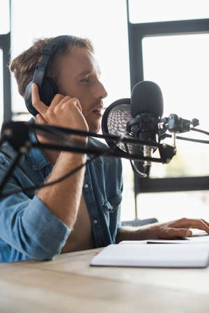side view of radio host adjusting headphones and talking while making podcast