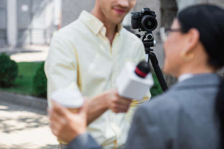 modern digital camera on tripod near blurred reporter taking interview with businesswoman