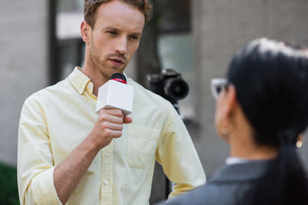 reporter holding microphone and talking near blurred businesswomanの写真素材