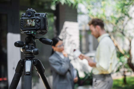 digital camera with reporter holding microphone while taking interview of asian businesswoman in...