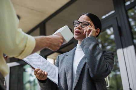 low angle view of reporter with microphone near pensive asian businesswoman adjusting glassesの写真素材