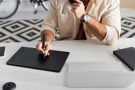 cropped view of retoucher drawing on graphic tablet near laptop on desk