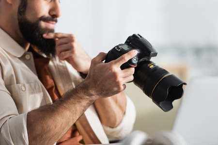 cropped view of thoughtful man touching beard while holding digital camera at home