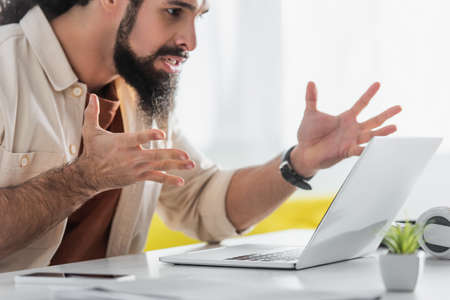 irritated hispanic freelancer gesturing near computer at homeの写真素材