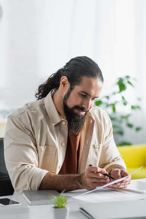 hispanic freelancer pointing with pen at document while working at homeの写真素材