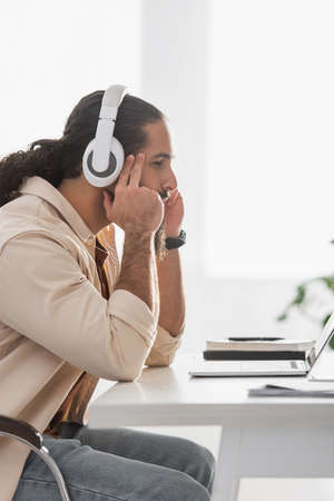 side view of focused latin freelancer in headphones looking at laptop during online webinarの写真素材