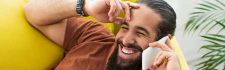 bearded latin man laughing while talking on mobile phone with closed eyes, bannerの写真素材
