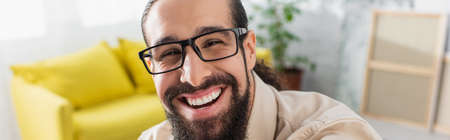 joyful hispanic man in eyeglasses laughing at camera, banner