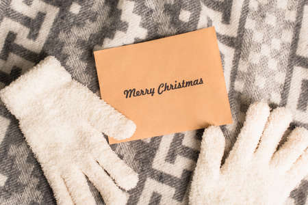 top view of warm gloves and greeting card with merry christmas lettering on grey blanket with...