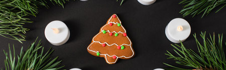 top view of gingerbread cookie near candles and pine branches on black, bannerの写真素材