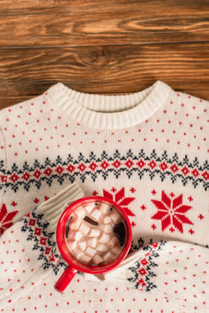 top view of cocoa with marshmallows on knitted sweater and wooden surface