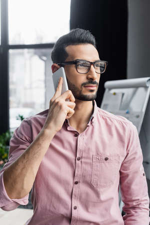 Muslim businessman in eyeglasses talking on smartphone in officeの写真素材