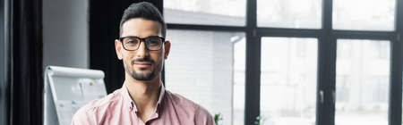 Arabian businessman in eyeglasses looking at camera in office, banner