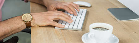 Cropped view of businessman using computer near cup of coffee in office, bannerの写真素材