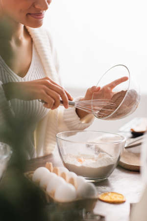 Cropped view of african american woman pouring cocoa in flour near blurred eggs in kitchen