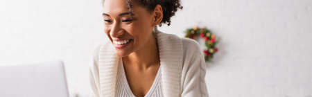 Positive african american woman using laptop during christmas at home, bannerの写真素材