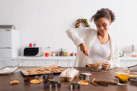 Smiling african american woman cooking near ingredients and christmas cookies in kitchen