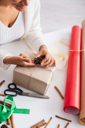 Cropped view of african american woman decorating present with pine cone near scissors at homeの写真素材
