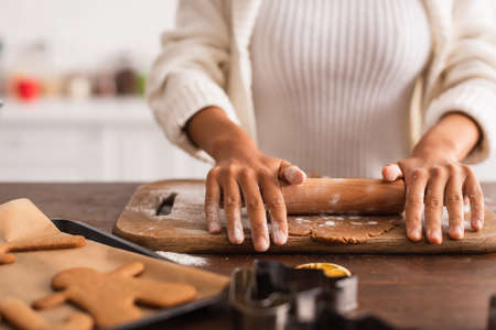 Cropped view of african american woman rolling dough near blurred christmas cookiesの写真素材