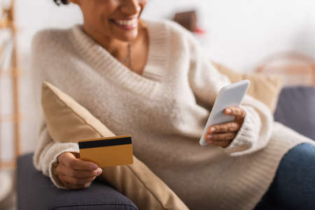 Cropped view of smiling african american woman using cellphone and credit card at homeの写真素材